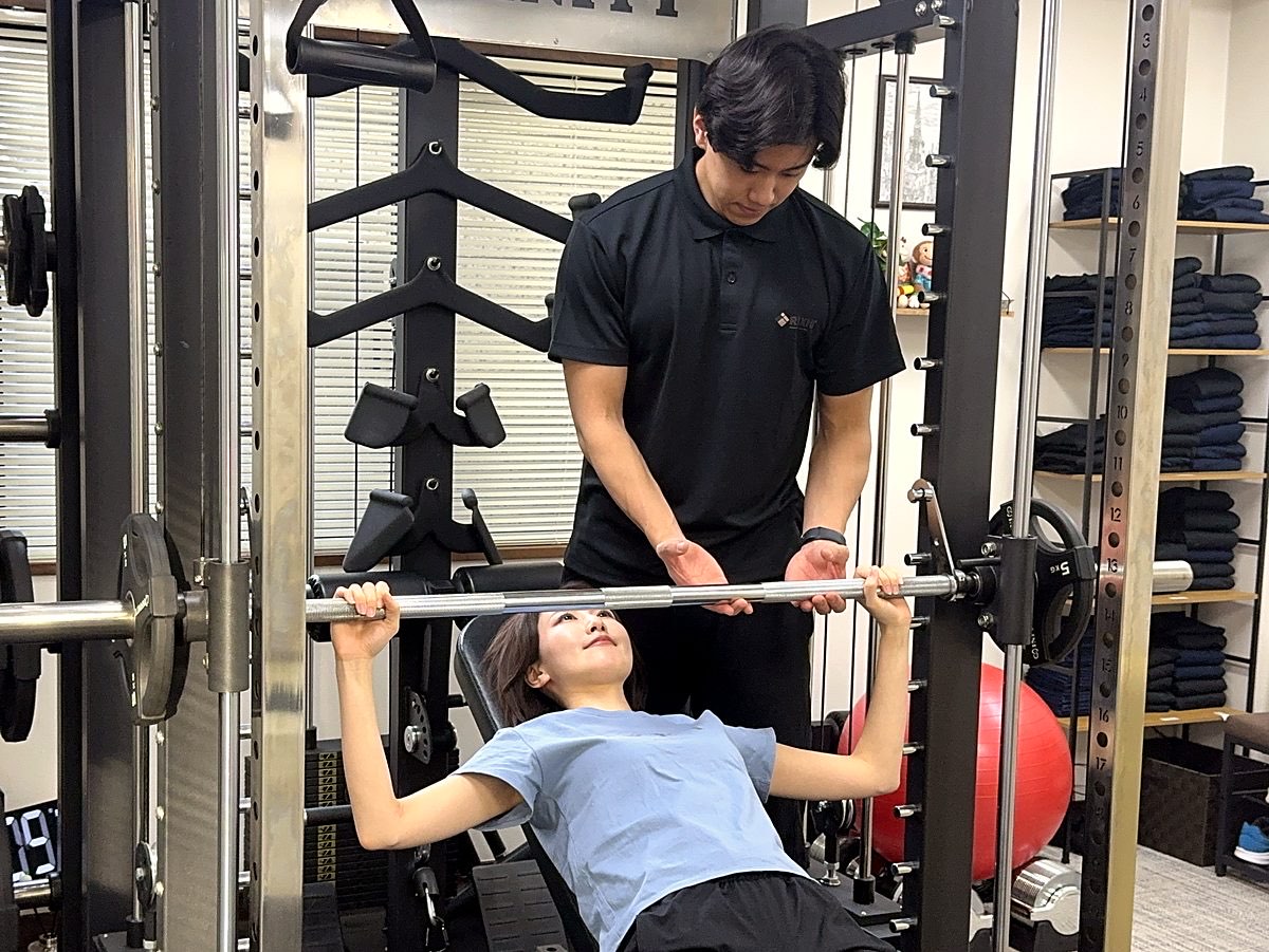トレーナーがお客様のベンチプレスを補助しながら指導している様子